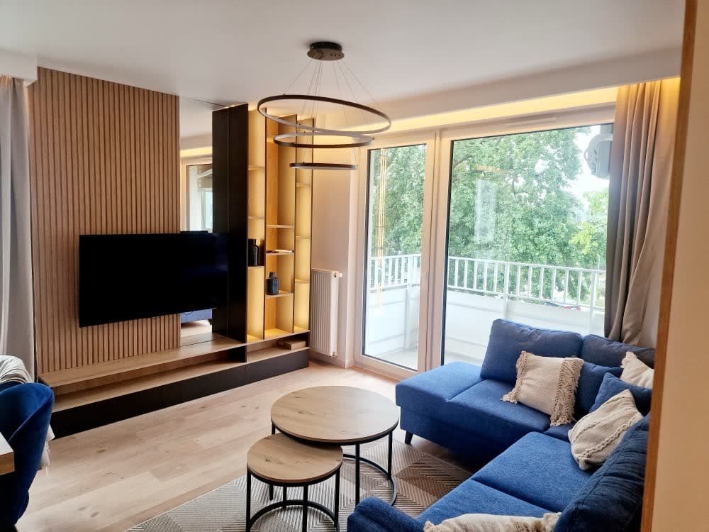 Salon z granatową sofą, ścianą telewizyjną i wyjściem na balkon