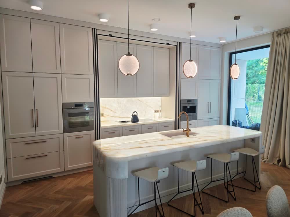 Kuchnia z wyspą z jasnego kamienia, drewniana zabudowa i lampy wiszące